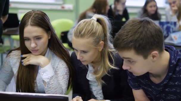 Grupo de estudiantes estudiando cuidadosamente la información en la pantalla del ordenador portátil. Otros estudiantes trabajan en el fondo. Proceso educativo en el aula de la universidad . — Vídeo de stock