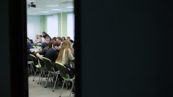 Grande grupo de pessoas em uma grande sala de aula leve sentadas na mesa e trabalhando juntas. Jovens economistas estão sentados à mesa discutindo a prática e esperando o início da palestra — Vídeo de Stock