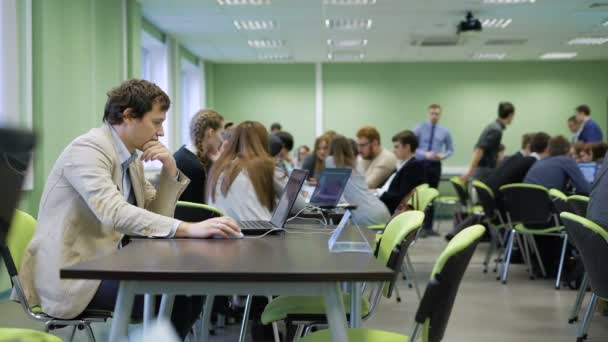 商务游戏的组织者坐在教室的桌子旁, 在学生们的房间里使用笔记本电脑, 正在按照游戏规则进行练习和扮演自己的角色. — 图库视频影像