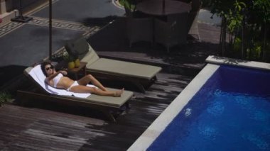 Otel bölgesi. Beyaz mayo bir tembel havuzun yanında yatan kız. Bu rahatlatır ve onların tatil günlerinde zevk alır. Güneş parlıyor Bali şehrinde hava durumu başarısız çünkü değil