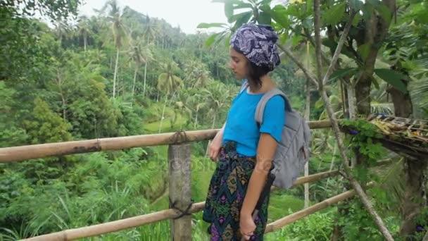 Европейская туристка, стоящая на террасе и смотрящая на пышную тропическую растительность. Молодая девушка самостоятельно исследует бесконечные балийские джунгли, хворост и рисовые поля . — стоковое видео
