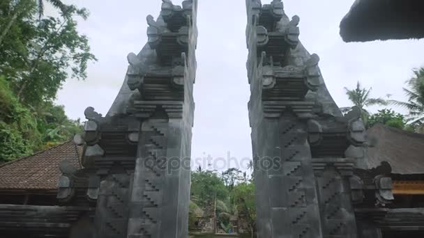 Ovanifrån ingången till en asiatisk tempel, som ligger i en tropisk skog med höga gröna palmer och andra träd, under en blå himmel genom ett stenvalv, som börjar med små steg — Stockvideo