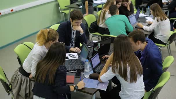 El equipo de jóvenes directivos se sienta junto a la mesa con ordenadores portátiles y se prepara para la presentación del proyecto. Tres chicas jóvenes y dos chicos — Vídeo de stock