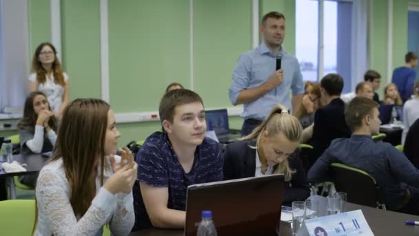 Equipo de jóvenes emprendedores sentados en el escritorio con portátil y preparándose para hacer la presentación de su nueva puesta en marcha de Internet a la audiencia, mientras que el orador — Vídeos de Stock