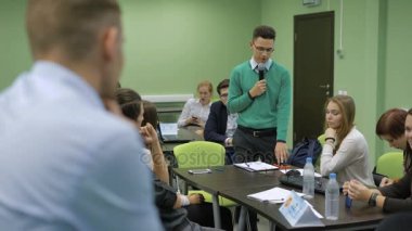 Yeşil gömlekli genç stuudent sınıfta ayakta ve mikrofona konuşan bir sınav geçiyor. Yüksek lisans çalışmaları hedef kitleye sunma hoparlör.