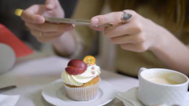Kadının el kahvesini kahve dükkanları tablo sosyal ağ için kafede oturan fotoğraf çekme kapuçino cupcakes yapıyorlardı. Akıllı telefon holding kadın eller