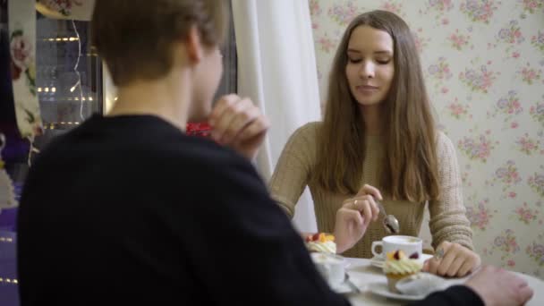 Sympatyczna para młodych ludzi w kawiarni rozmawiać. Dziewczyna uśmiecha się chłopakiem, pije kawę, ciepłe ręce. Piękna Brunetka trochę mylić i w miłości. — Wideo stockowe