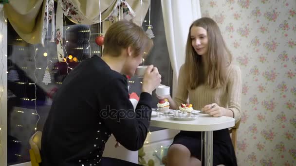 Nice couple of young people in the cafe talk. Girl smiling at her boyfriend, she drinks coffee, warm hands. Beautiful brunette little bit confused and in love. — Stock Video