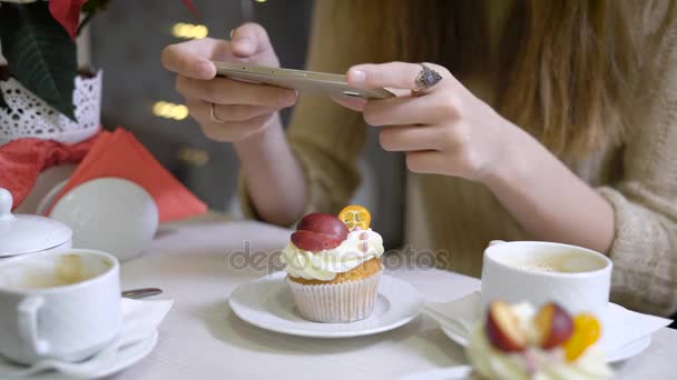 Kadının el kahvesini kahve dükkanları tablo sosyal ağ için kafede oturan fotoğraf çekme kapuçino cupcakes yapıyorlardı. Akıllı telefon holding kadın eller — Stok video