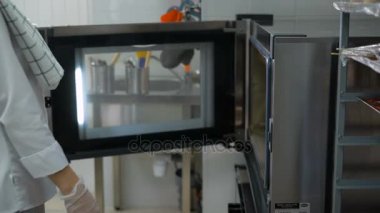 Bir şekerci dükkânı kadında. Kız beyaz bir form ve renksiz eldiven ve gri pantolon hamur ekmek makinesi fırın için bir fırın tepsisine yerleştirilir.