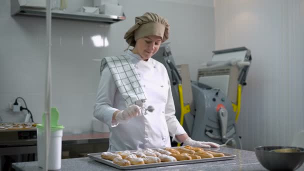 Professionelle Süßwaren mit Puderzucker bestreut frisch gebackene eclair in der Küche in der Bäckerei. Ausrüstung für die Zubereitung von Süßigkeiten im Hintergrund. — Stockvideo