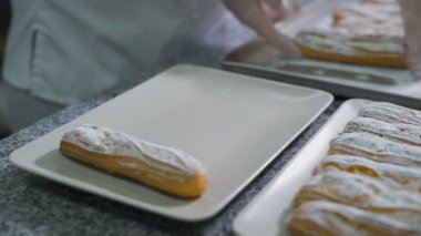 Fırından yeni çıkmış ekmek mutfakta güzel bir beyaz Tabaklarda pudra şekeri ile eklerleri Baker düzgünce katlanmış ellerinizle. Masanın üzerinde birçok lezzetli kek.