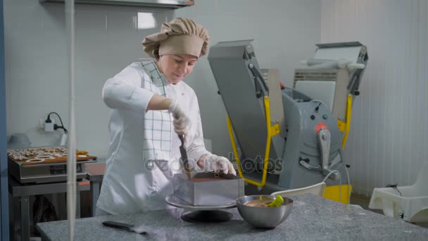 Mujer seria de pie detrás de la mesa de pastelería povarsikim en el fondo de la confitería cosechadora mecánica y los cortes de pala de pastel de chocolate del molde de metal y luego eliminarlo — Vídeos de Stock