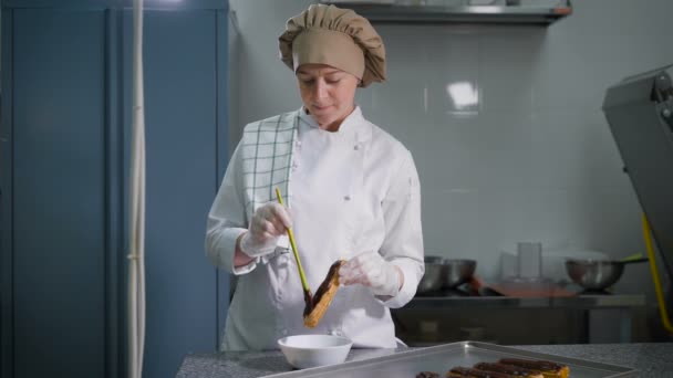 Dikke laag chocolade uitstrijkjes banketbakker zachtjes op versgebakken eclairs. Professionele chef-kok tijdens haar favoriete werk. Apparatuur voor de bereiding van zoetigheden. — Stockvideo
