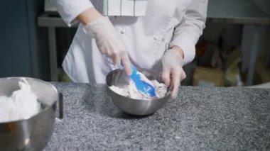 Baker lezzetli Kurabiye hazırlanması için metal bir kase hamur karışımları. Mutfak alt beyaz üniforma ve tek kullanımlık eldiven.