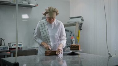 Kız beyaz üniformalı düzgünce ekmek mutfakta üç eşit parçaya çikolatalı pasta keser. Baker tarafına bakarak iş başında.
