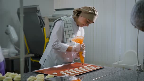 Algunos pasteleros trabajando en una tienda de dulces. Una de las mujeres involucradas en la creación de pasta. Usar una bolsita de pastelería empuja los círculos sobre una mesa — Vídeos de Stock