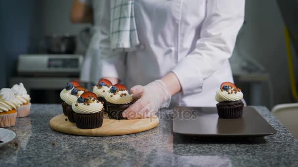 Cook zet op een bruin bord met vers gebakken muffins mee te nemen naar de client. Zeer mooie en heerlijke zoetigheden. Professionele productie van desserts. — Stockvideo