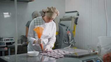 Pudra taze pişmiş çerezleri kullanarak Pasta krema döker. Kız beyaz üniformalı tatlı pişirmeye bayılır. Yardımcısı cook kek arka planda formları hazırlar.