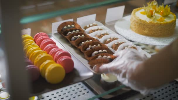 Verkoper met de hand nemen sommige prachtige en heerlijke cookies om te verkopen aan de koper. Op venster beeldscherm een groot aantal multi-gekleurde snoepjes. Meesterwerken van de culinaire kunst close-up. — Stockvideo