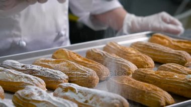 Pasta şefi, giyinmiş bir beyaz şefler takım elbise ve özel bir fincan - metal bir tepsi üzerinde duran eklerleri pişirmek bir elek pudra şekeri serpin şeffaf eldiven