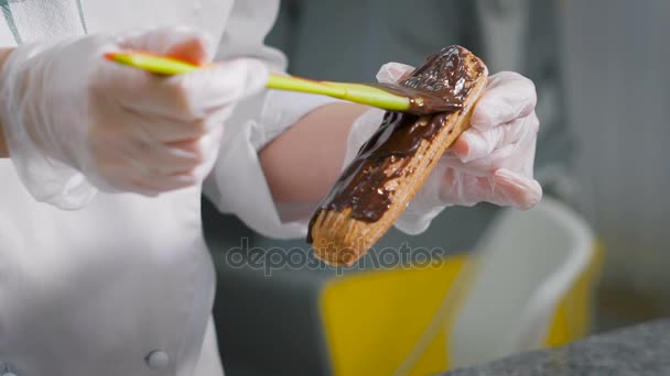 Cukrász óvatosan kenetet vastag réteg csokoládé a frissen sült eclairs. Profi szakács kedvenc munkája során. Folyékony tejszín csepp esett le. — Stock videók