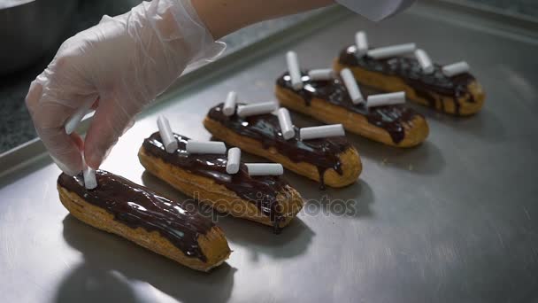 Cuocere delicatamente decorato con eclairs di cioccolato appena sfornati utilizzando meringa. Pasticcere sapientemente fare un capolavoro culinario . — Video Stock