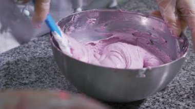 Pastacı, eldiven tarafından korunan elleri yavaş yavaş pembe badem ezmesi mavi silikon kaşık yardımı ile karışımları.