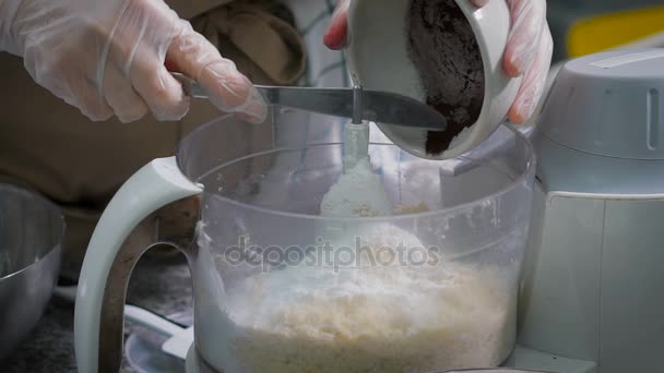 Konditorn häller försiktigt den hackade chokladen i en bunke. I mixer stort antal ingredienser för att göra godis. Kocken arbetar i handskar. — Stockvideo