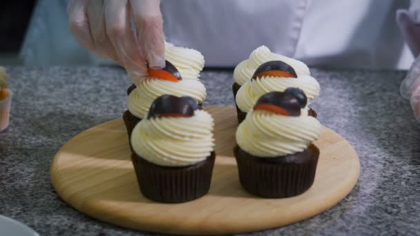 Confeitaria. A menina está se preparando para o feriado cupcakes personalizados. Os queques estão prontos na mesa. Acabamentos de confeiteiro executar cupcakes de chocolate. Mulher decora cupcakes fruta . — Vídeo de Stock