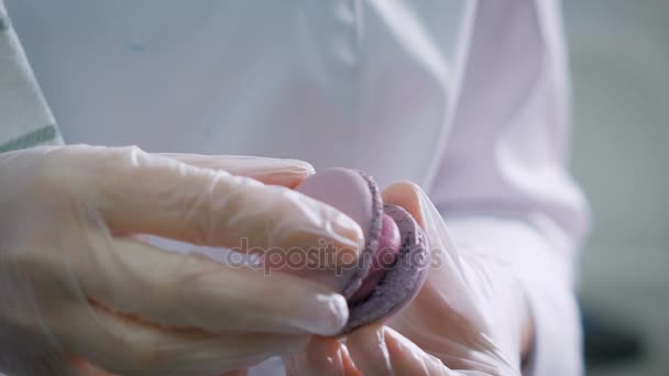 Konditor verbindet die beiden Hälften eines Keks, zwischen denen sich eine Creme befindet. Süßigkeiten, die vom Konditor in einer professionellen Küche hergestellt werden. Köchin macht schöne Desserts mit ihren eigenen Händen. — Stockvideo