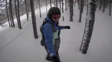 Kalın bir sakallı bir adam aktif bir snowboard karlı bir ormandaki üzerindeki küçük kar engeller gezdi. Sırt sırt çantası ile gerekli şeyleri tartmak