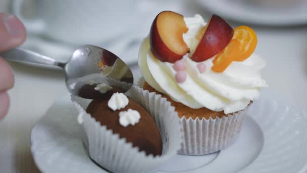 Ο άνθρωπος απαλά και σιγά-σιγά έσπασε ένα μικρό κομμάτι του καφέ γλυκό κέικ, το οποίο βρίσκεται σε ένα πιάτο με ένα όμορφα cupcakes διακοσμημένα με κρέμα και φρούτα κομμάτια βουτύρου — Αρχείο Βίντεο
