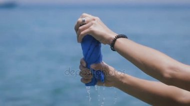 Eller genç kadının Bali beach adanın Yüzme sonra mavi havlu sıkma kapatın. Kadın Gezgin ile bilezik ve havlu kumaş tutarak ve deniz arka planda basarak çalmak.