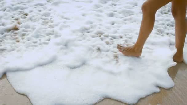 Nahaufnahme von schönen, sexy gebräunten Frauenbeinen, die auf dem Sand spazieren und ins Meer steigen. Bild von Wellen, die auf die Küste kommen und weiblichen sockenlosen Füßen, die im schäumenden Ozean gehen. — Stockvideo