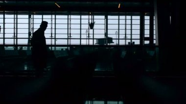 Havaalanındaki yürüyen merdiven üzerinde binen bir adam şapkalı bir silueti. Arka planda büyük bir pencere. Günlük yaşamda modern teknoloji.