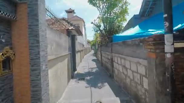 Обзор местности на Бали. В районе дома из камня, зеленые пальмы, железные ворота, бетонные стены и узкие дорогие — стоковое видео
