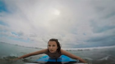 Bali Adası. Okyanus. Genç esmer bir sörf tahtası üzerinde beyaz bir kaplnik içinde. Kız bir dalga yakalamaya çalışır. Kadın bir gemide kalkar ve bakiye tutar, ama sonra dalga onu suya atar.