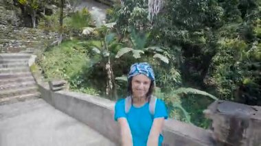 Bali Adası. Adada bir gezi. Kız mavi gömlekli taş köprünün üzerinde yürür. Alan ve kendisi bir selfie sopa video aracılığıyla esmer vuruyor. Kız büyük ruh hali