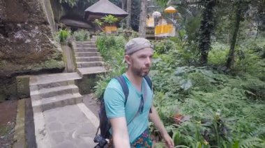 Bali Adası. Adada bir gezi. Mavi gömlekli ve omuzlarında bir sırt çantası ile kişi taş bir patika üzerinde yürüyor. Bir selfie için bir sopa video aracılığıyla adam vuruyor.
