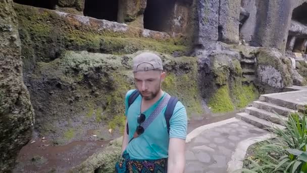 Viajero masculino explorando los alrededores del antiguo templo balinés a pie sosteniendo selfie-stick en sus manos. Hombre barbudo caminando por las escaleras tomando fotos de la selva tropical con el camino detrás de él . — Vídeo de stock