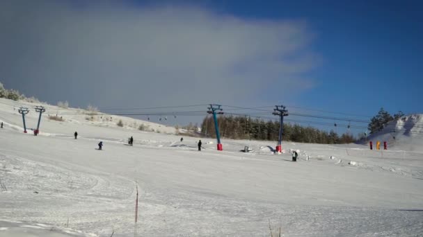 Вид на горнолыжный склон. Зима на улице и холодная погода, поэтому катающиеся на лыжах сноубордисты тепло одеты. Издалека можно увидеть лес с деревьев . — стоковое видео