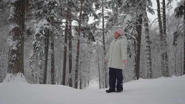 Dospělé ženy v zimním lese. Důchodce má zbytek. Věku v kombinéze obdivuje krásy lesa. Chůze je velmi užitečné pro zdraví. — Stock video