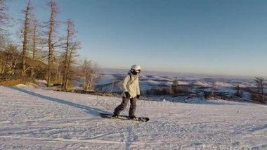Snowboard aşağı Kayak, dağ yamacında güneşli frost gününde kayıyor. Kız Kayak kıyafeti ve kask içinde hızlı bir şekilde yokuş aşağı karla kaplı tepeleri ve ağaçlar içinde belgili tanımlık geçmiş ile gidiyor.