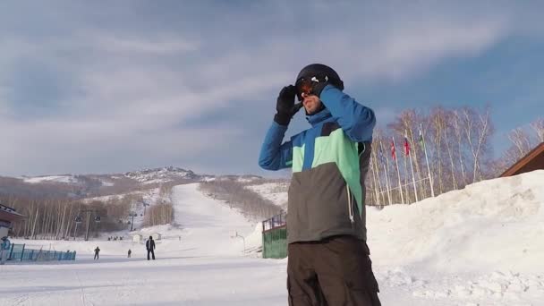 Estância de esqui. O snowboarder ajusta os óculos e um capacete e tem um resto, prepara-se para a seguinte chegada. O homem está vestido com um terno de esqui especial que permite um longo tempo — Vídeo de Stock