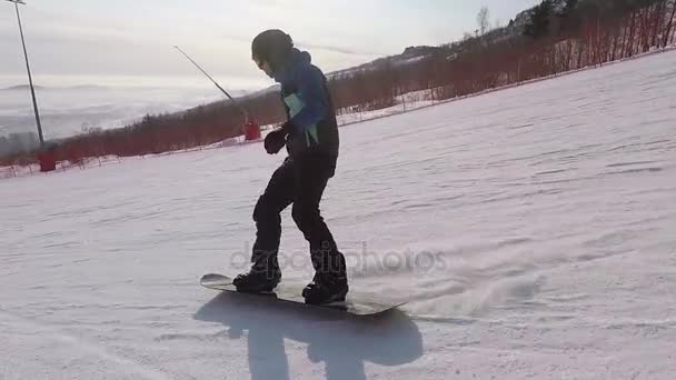 El snowboarder en la estación de esquí. El atleta corta en la tabla de snowboard en la nieve en un clima soleado. El hombre está vestido con un traje especial para el snowboarder. — Vídeo de stock