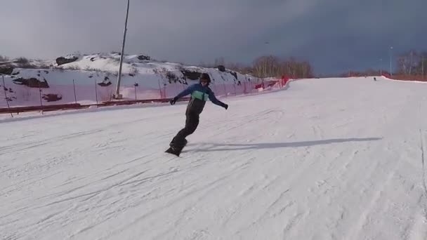 Snowboarder ιππασία πάνω από την πλαγιά στα βουνά. Νεαρός άνδρας ντυμένος με κοστούμι σκι είναι χαρούμενος που αυτός έχει καλά τυλιγμένος σε ένα snowboard. Επιτυχείς άνθρωποι δραστήριες διακοπές. — Αρχείο Βίντεο