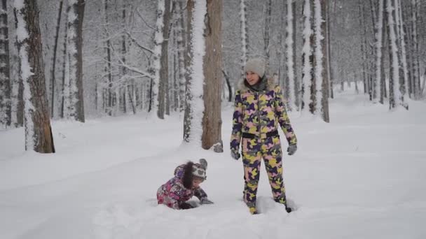 Lycklig familj av ung mamma och lilla dotter spela tillsammans och ha roligt i vinter naturen utomhus i skogen. Ung kvinna ler och faller ner i snödriva tillsammans med flickan. — Stockvideo