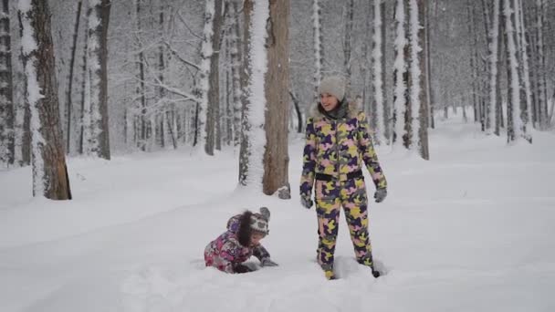 Szczęśliwa rodzina młoda matka i małą córeczkę, gry i zabawy w naturze zimą na zewnątrz w lesie. Młoda kobieta uśmiechając się i spada w dół w zaspie wraz z dziewczyna. — Wideo stockowe