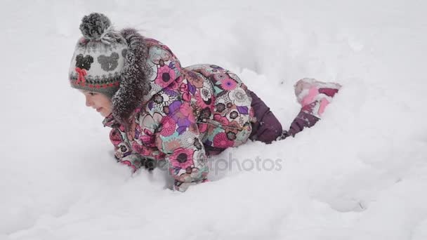Маленькая девочка в розовом ботинок, яркая куртка и кепка с помпоном дурачиться в снегу. Она любит зиму и играет в парке с родителями. . — стоковое видео